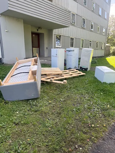 Avfall og hvitevarer på gressplenen utenfor en bygning